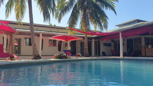 a swimming pool in front of a house with palm trees at Villa Les Cocotiers in Nosy Be