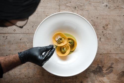 a person in black gloves holding a plate with yellow peppers at Boutique Hotel Eschenlohe in Schenna
