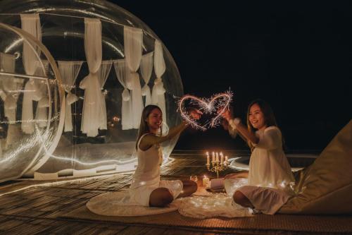 deux femmes assises sur le sol et tenant un cœur avec des étincelles dans l'établissement The Three Bubble Houses, à Sai Yok