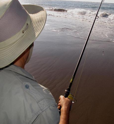 a man in a hat holding a fishing pole on the beach at Puerto Barillas in Bahia de Jiquilisco