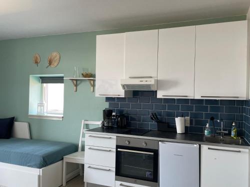 a kitchen with white cabinets and a blue tiled wall at Havudsigt, skøn lille lejlighed in Tranekær