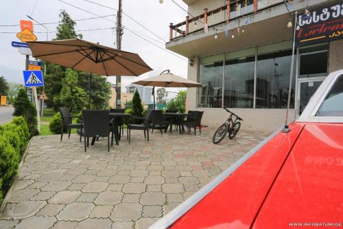 eine Terrasse mit Tischen, Stühlen und einem Sonnenschirm in der Unterkunft Hotel CARLEONE in Batumi