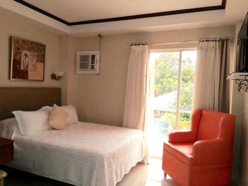 um quarto com uma cama, uma cadeira e uma janela em Aberrise Country Villa Pension Hotel em Dumaguete