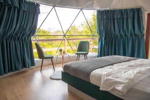 a bedroom with a bed and two chairs and a large window at Sanctum Glamping in Jupâneşti