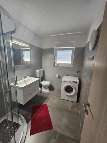 a bathroom with a toilet sink and a washing machine at Apartmani Viktorija in Fažana
