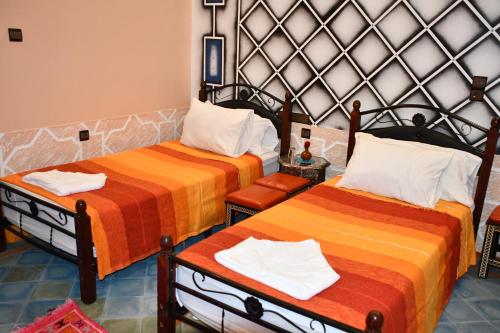 una camera con due letti con lenzuola arancioni e arancioni di Hôtel La Vallée Des Oiseaux a Boumalne Dades