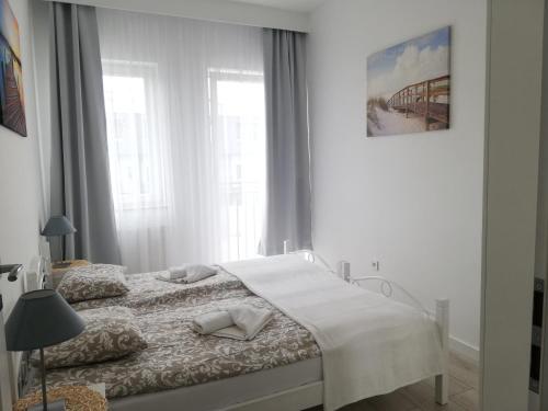 a white bedroom with a bed in a room with windows at Apartament Kapitalny in Dziwnówek