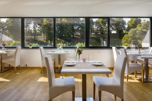 um restaurante com mesas e cadeiras brancas e janelas em Hotel Lara em Valença