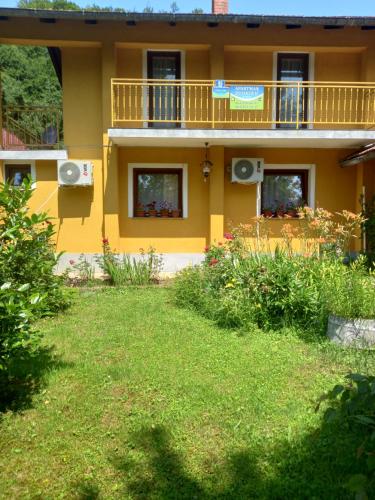 a yellow house with a balcony and a yard at Soba Dujaković in Banja Vrućica