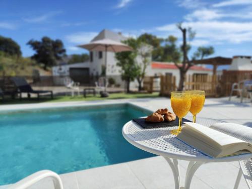 einen Tisch mit zwei Gläsern und ein Buch neben einem Pool in der Unterkunft Casa de campo con maravillosas vistas, bbq y piscina in Ronda