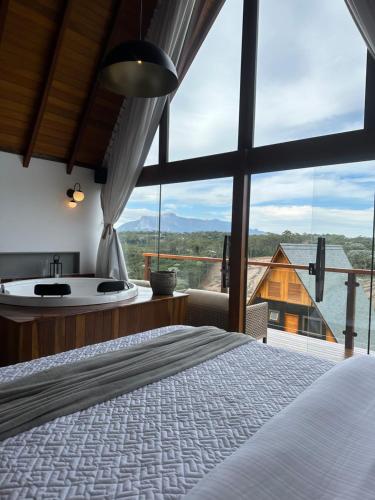 a bedroom with a tub and a bed and a large window at Chalés Laguna Alto Viçosa in Venda Nova do Imigrante