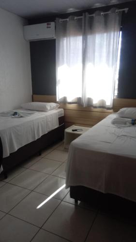 a hotel room with two beds and a window at Hotel Copacabana in Araucária