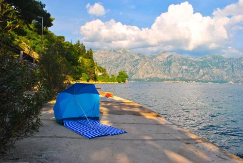 a blue umbrella sitting on a sidewalk next to a body of water at Apartment Mediterraneo Blue Sky in Perast