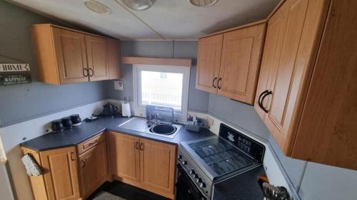 a small kitchen with wooden cabinets and a sink at Millfields 6 berth caravan MAX 4 ADULTS Bob family's only and lead person must be over 30 in Ingoldmells