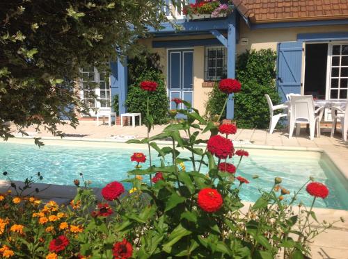 a house with a swimming pool with red flowers at La Maison Bleue Normande in Maniquerville