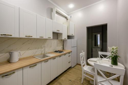 a kitchen with white cabinets and a sink and a table at Апартаменти на Кобилянській by Willox in Chernivtsi
