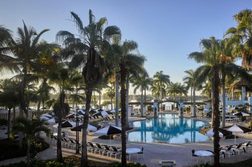 vistas a una piscina con palmeras y sombrillas en The Cottages at PGA National Resort, en Palm Beach Gardens