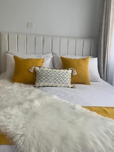 Cama blanca con almohadas amarillas y manta blanca en Sky Nest Grey point 306, en Kericho