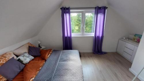 1 dormitorio con cortinas moradas, 1 cama y ventana en Zielony Zakątek Demlin, en Demlin