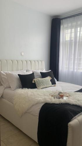 ein weißes Bett mit schwarzen und weißen Kissen und einem Fenster in der Unterkunft Grey Nest Grey point 303 in Kericho