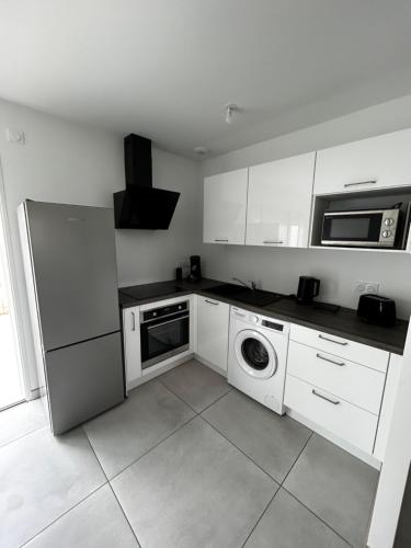 a kitchen with white cabinets and a washer and dryer at Maison neuve à 13 min des Sables in Talmont