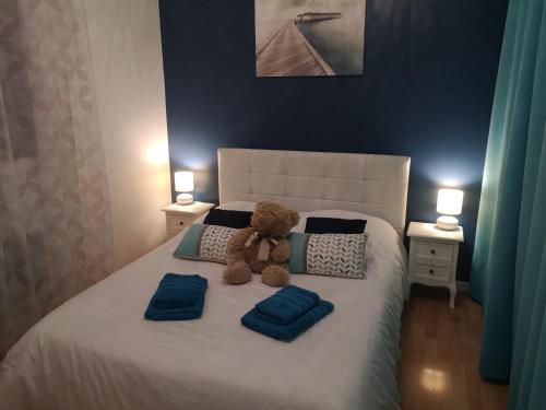 un osito de peluche sentado en una cama con almohadas azules en La Roseraie, en Tonneins