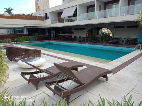 uma piscina com duas cadeiras e uma mesa ao lado de um edifício em Loft Encantador, a beira mar! em Salvador