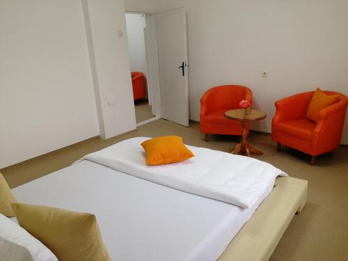 a room with a bed with an orange pillow and two chairs at Apartman Mušinbegović in Visoko