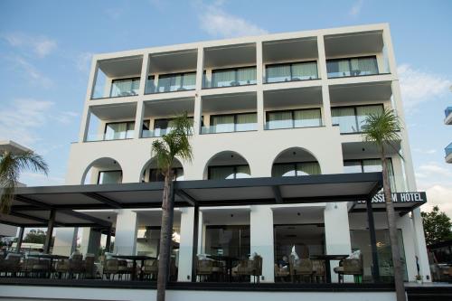 a white building with palm trees in front of it at Colosseum Hotel in Ksamil