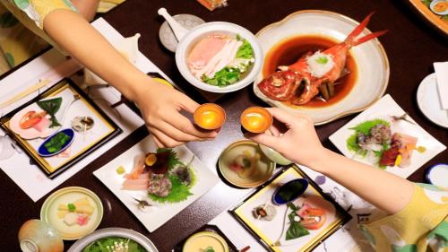 two people holding food on a table with plates of food at Yuyado Mikannoki in Atami