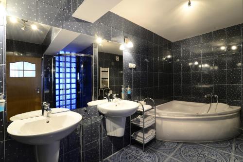 La salle de bains est pourvue de carrelage noir, de deux lavabos et d'une baignoire. dans l'établissement Hotel IKAR, à Bydgoszcz