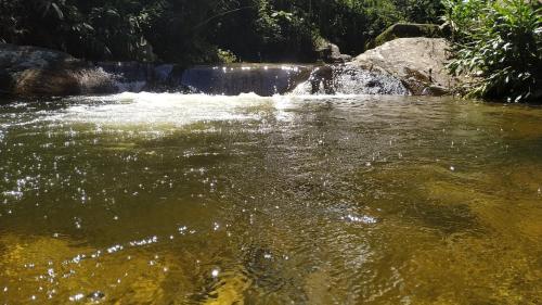 a stream of water with a waterfall in the background at Casa do Cedro - Sítio Cascatinha in Cruzeiro