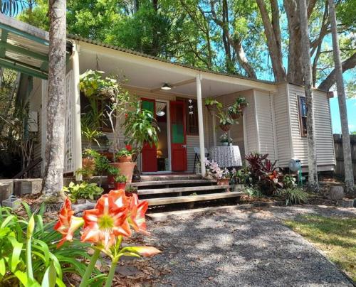 a white house with a red door and some flowers at Quirky Cottage in Centre of Maleny, Walk Everywhere in Maleny