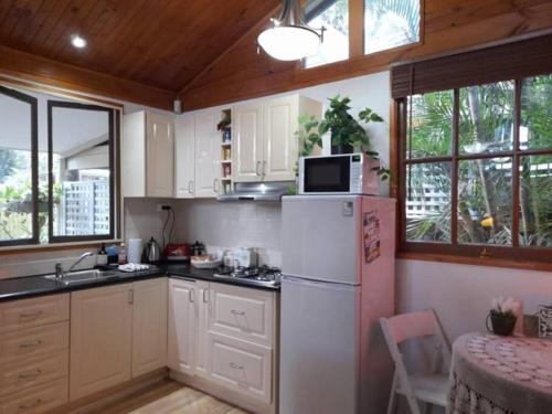 Il comprend une cuisine équipée d'un réfrigérateur, d'une table et de fenêtres. dans l'établissement Quirky Cottage in Centre of Maleny, Walk Everywhere, à Maleny