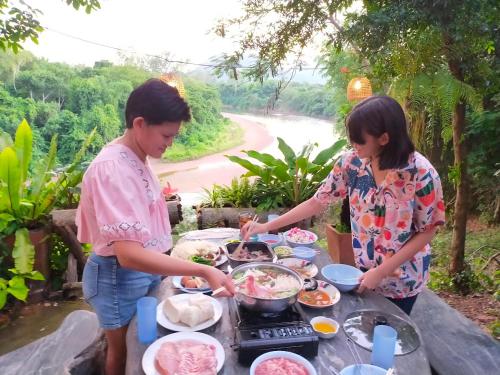 un hombre y una mujer preparando comida en una mesa en Baanmai Phaipa House, en Sai Yok