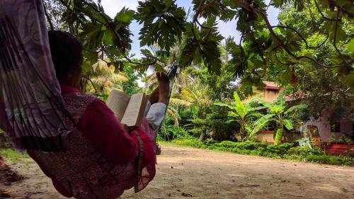 a woman reading a book under a tree at Marari Bethsaida Homestay in Shertallai