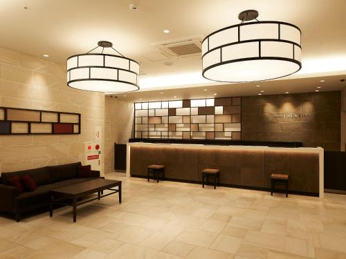 a lobby with a waiting area with a couch and two lights at Sotetsu Fresa Inn Kitahama in Osaka