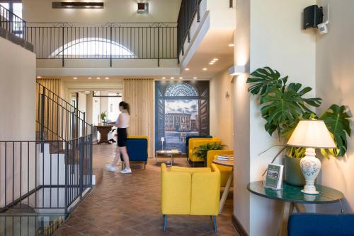 a woman walking through a lobby with yellow chairs at Nèroli Bio Relais in Catania