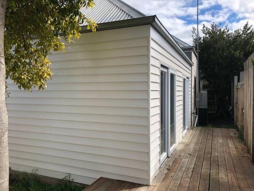 a white building with a wooden walkway next to it at Beach House of Queenscliff in Queenscliff
