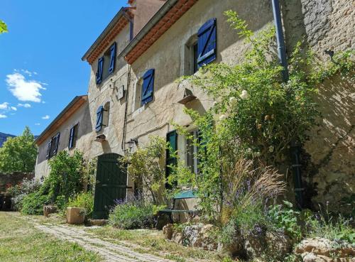 an old stone house with blue windows and a yard at Véritable Mas Provençal À La Palud in La Palud sur Verdon