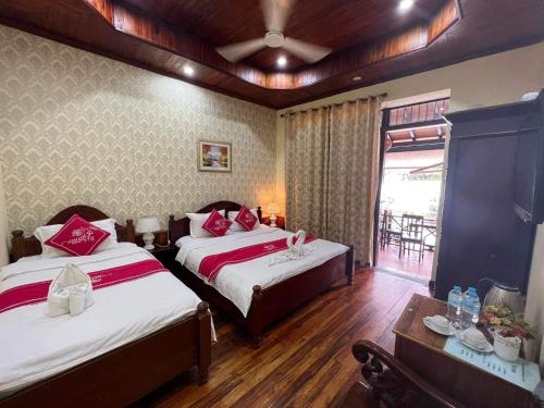 a bedroom with two beds and a table and a window at Villa Phathana Royal View Hotel in Luang Prabang