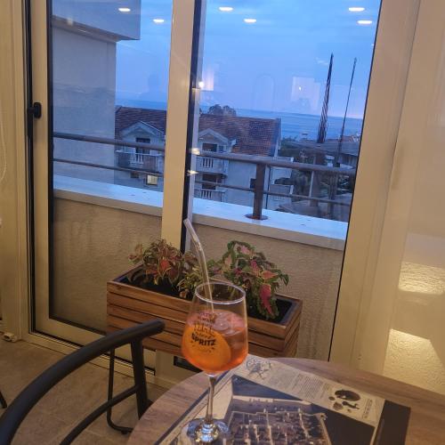 a glass of wine sitting on a table in front of a window at Apartmani Marina Kopitovic in Petrovac na Moru