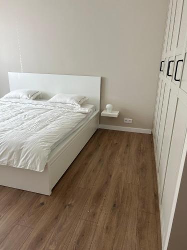 a bedroom with a white bed and wooden floors at Skandi Appartments in Saldus city center in Saldus