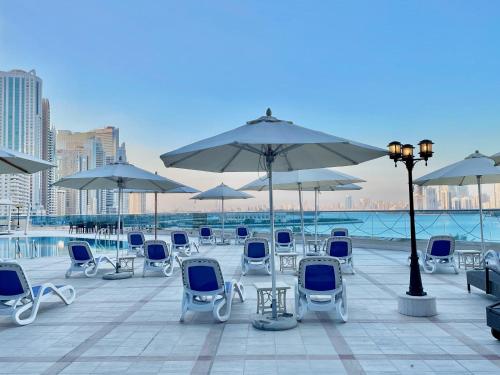 Corniche Hotel Sharjah في الشارقة: مجموعة من الكراسي والمظلات على الفناء