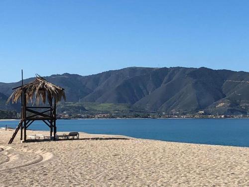 a bench on a beach with a straw umbrella and water at Portorosa in Torre Forte