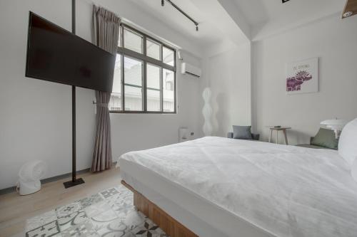 a white bedroom with a large bed and a window at Long Stay Here in Tainan