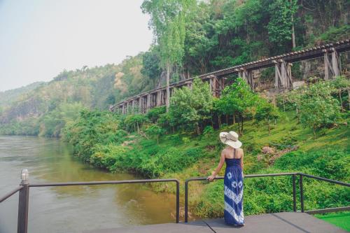 a woman standing next to a railing looking at a river at Suan Sai Yok Resort in Sai Yok