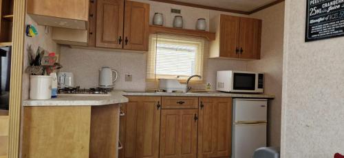a small kitchen with wooden cabinets and a microwave at 2 bed 36 Highbury park Skegness ingoldmells caravan in Ingoldmells