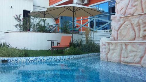 uma piscina com um guarda-sol, uma cadeira e uma mesa em Sapar Budget Hotel em Shymkent
