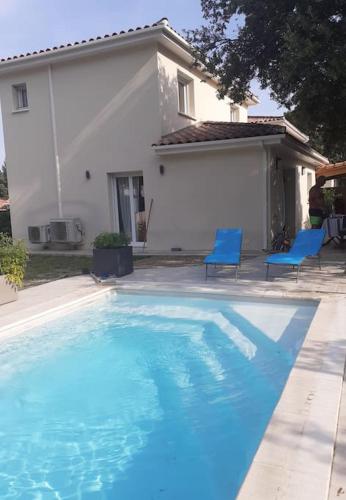 une piscine avec deux chaises bleues et une maison dans l'établissement Maison familiale cosy., à Saint-Bauzille-de-Montmel